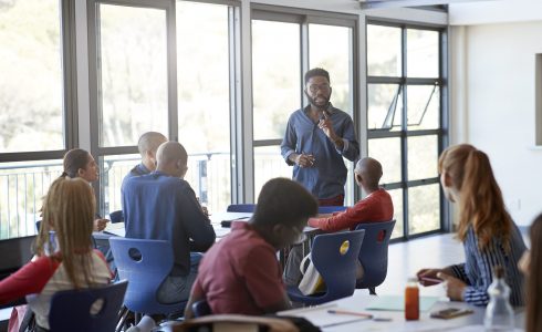 Confident young male professor explaining multi-ethnic students in community college classroom
